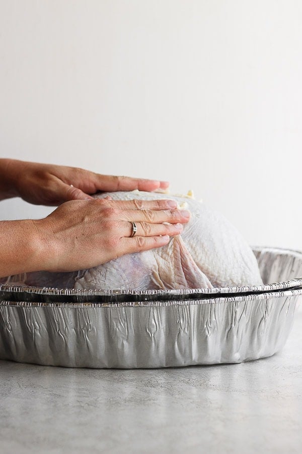 Someone rubbing butter all over a whole turkey.