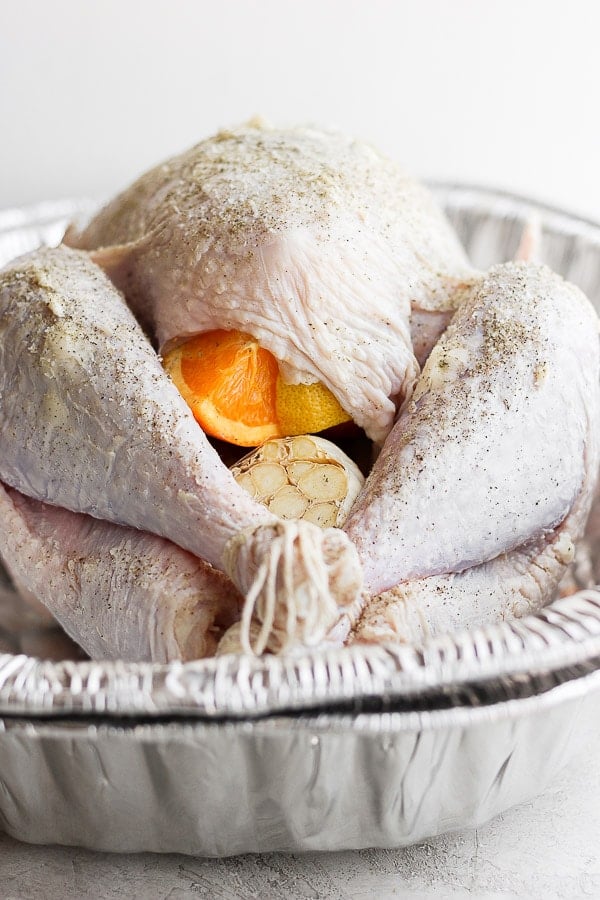 The front of a whole, raw turkey showing some orange and garlic stuffed inside and ready to go on the grill. 