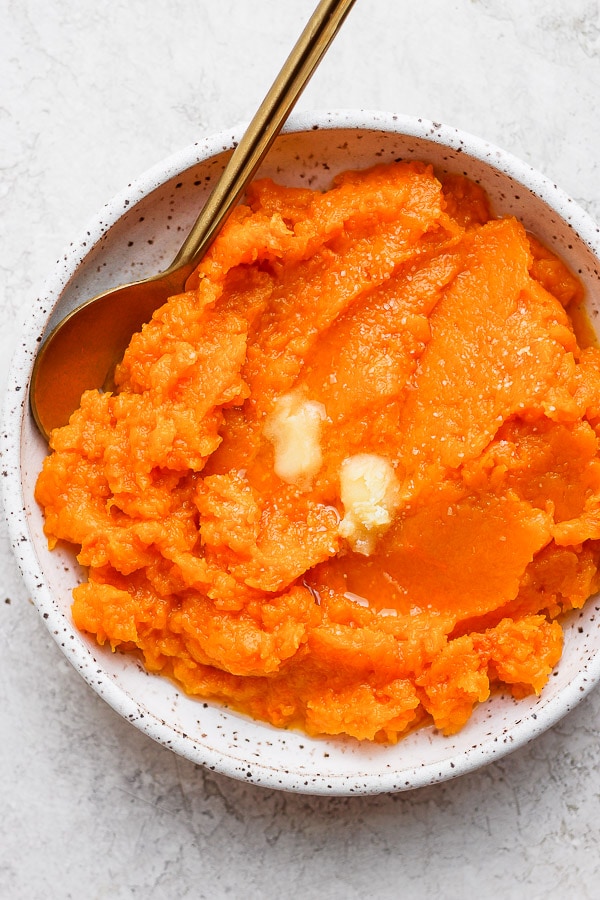 A plate of butternut squash mash with some butter on top and a spoon.