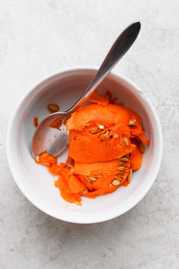 Butternut squash seeds and strings in a small bowl with a spoon.