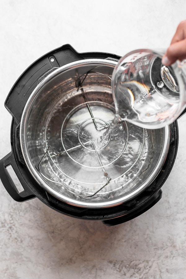 Water being poured into the bottom of an Instant Pot with the trivet on the bottom.
