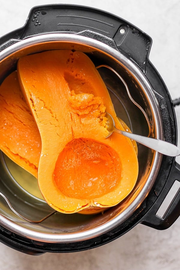 A spoon beginning to scoop the butternut squash meat out of the skin.