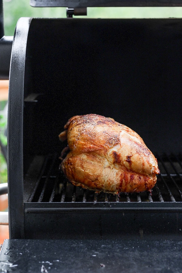 A cooked, brown turkey breast sitting on the grates of an open smoker. 