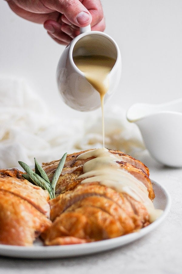 Turkey gravy is being poured on slices of cooked turkey on a plate.