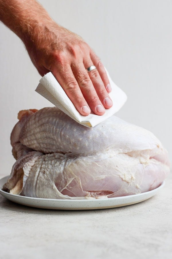 A hand patting dry a raw turkey breast with a paper towel. 