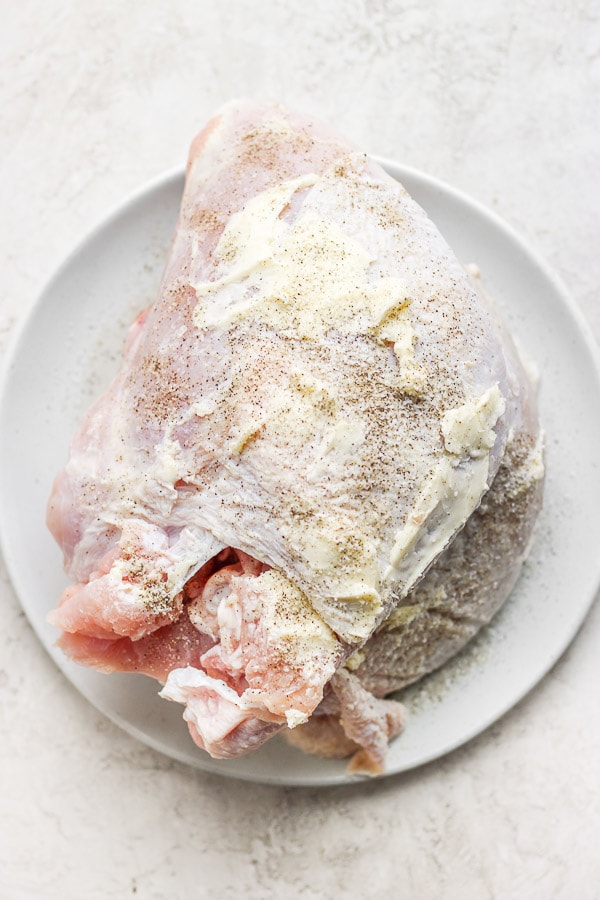 Top down shot of a raw turkey breast that is covered in soft butter and seasoned with salt and pepper. 