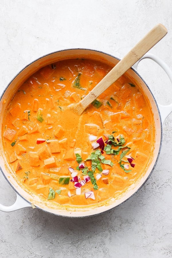 Sweet potato curry in a dutch oven with a wooden spoon.