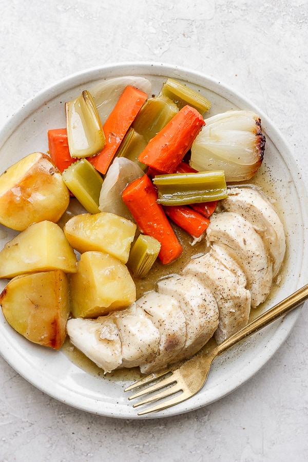 Plate of chicken, potatoes and veggies covered in gravy. 