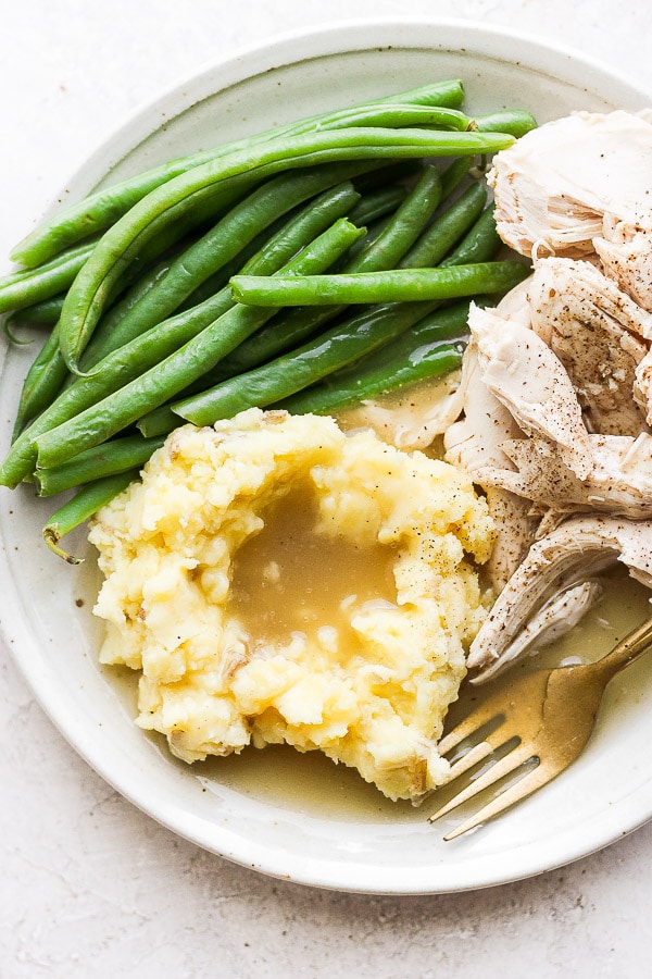 Plate filled with steamed green beans, mashed potatoes and gravy and chicken. 