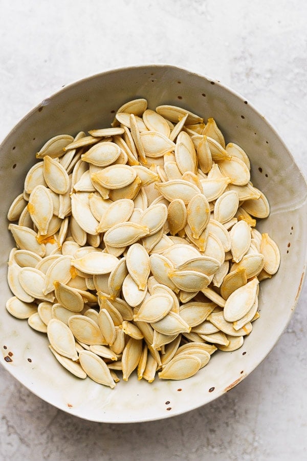 Bowl with pumpkin seeds that have been removed from a large pumpkin.