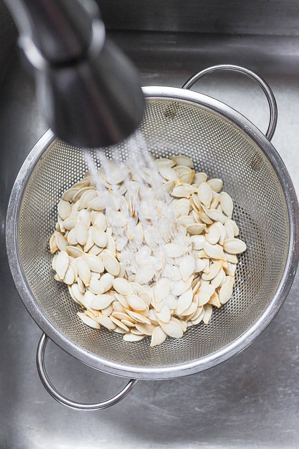 Pumpkin seeds being rinsed in a colander in a sink to remove any pumpkin on them.