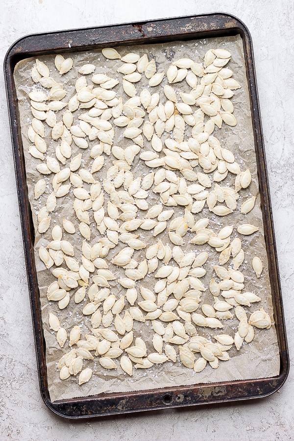 Rinsed pumpkin seeds on a parchment-lined baking sheet and sprinkled with generous amounts of salt.