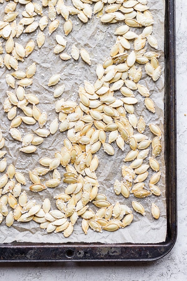 Pumpkin seeds on a parchment-lined baking sheet that has been roasted in the oven.