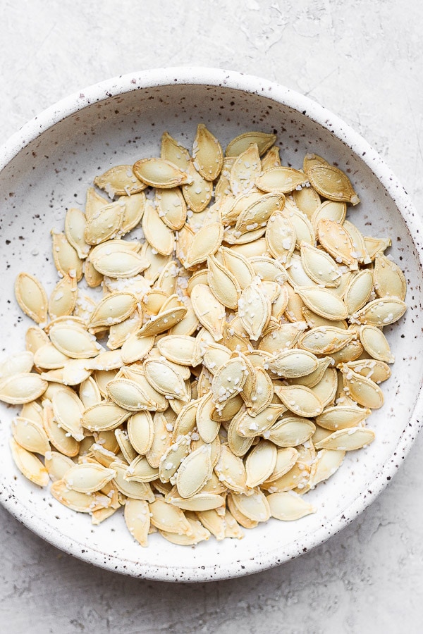 Roasted pumpkin seeds with generous amounts of salt in a shallow bowl.