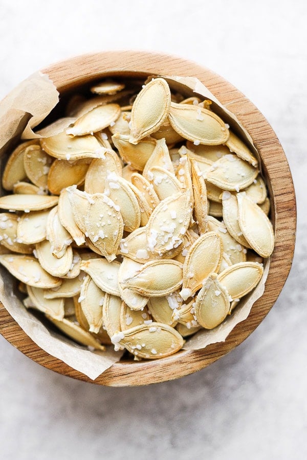 Wood bowl filled with roasted pumpkin seeds and sprinkled with salt.