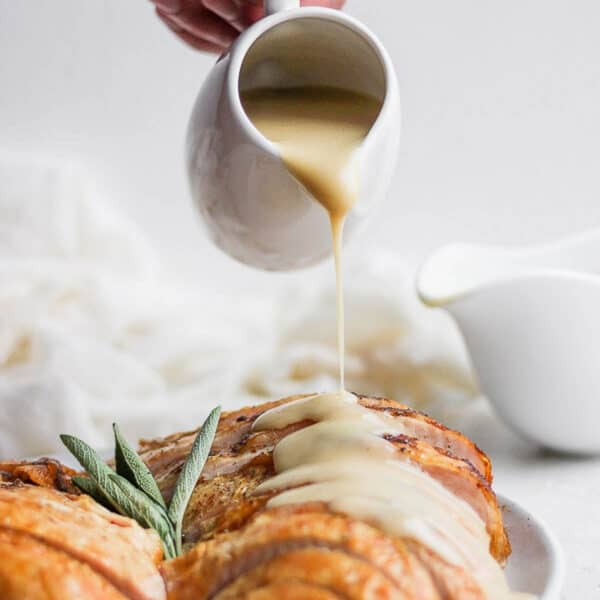 Someone pouring homemade turkey gravy over a sliced turkey breast.