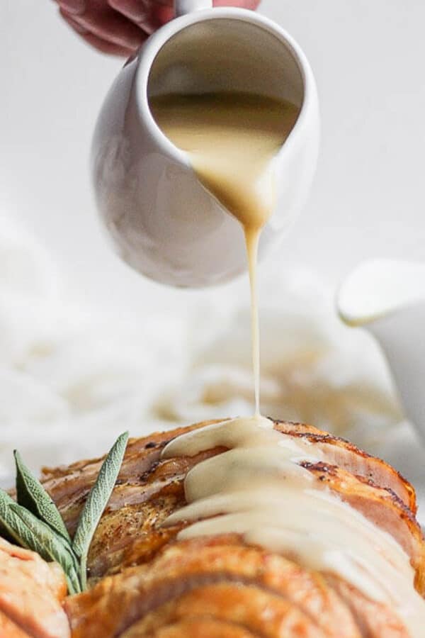 Someone pouring homemade turkey gravy over a sliced turkey breast.