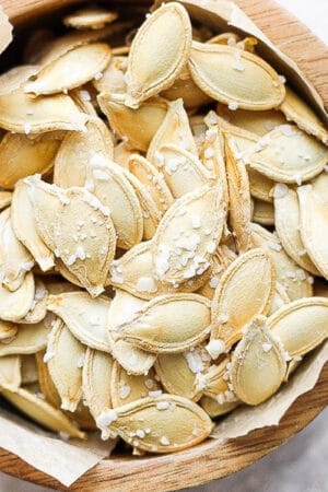 A wooden bowl lined with parchment filled with roasted and salted pumpkin seeds.