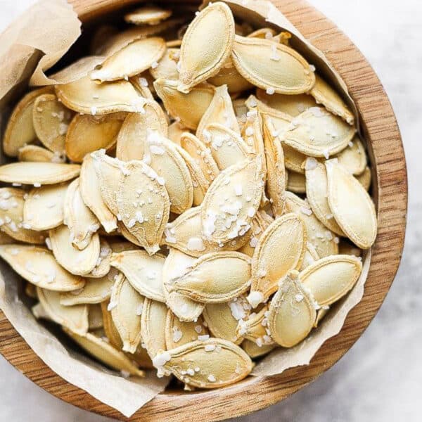 A wooden bowl lined with parchment filled with roasted and salted pumpkin seeds.