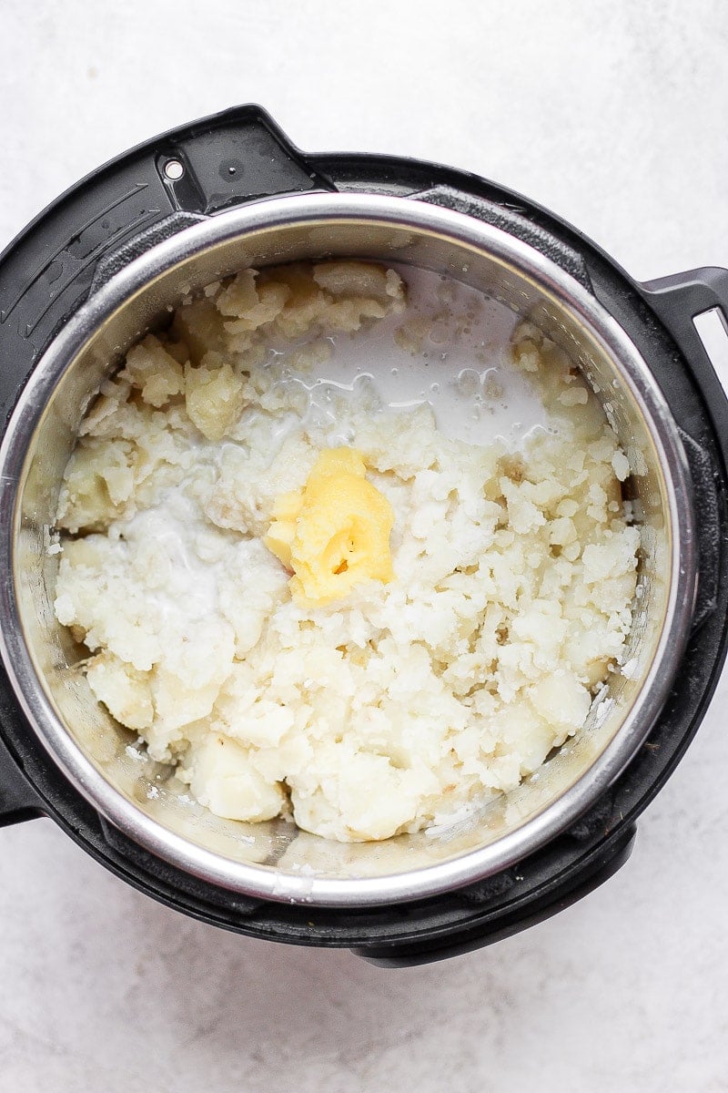An Instant Pot with partially mashed potatoes plus ghee, coconut milk, and garlic.