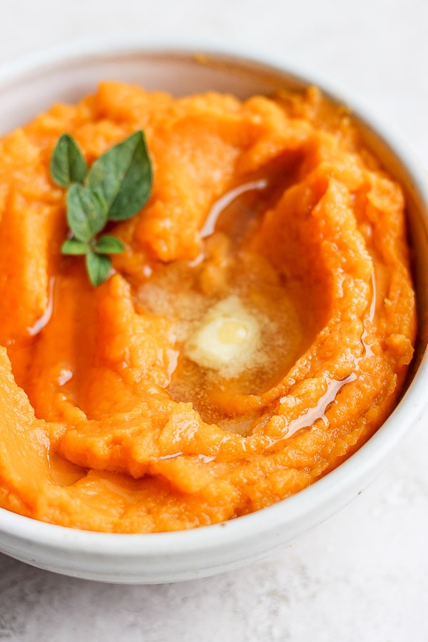 Mashed sweet potatoes in a bowl with melted ghee on top.