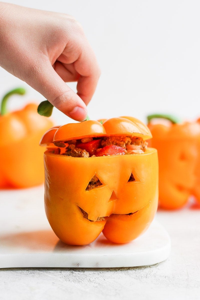 A jack-o-lantern stuffed pepper with a hand lifting the top slightly so you can see the stuffing inside.