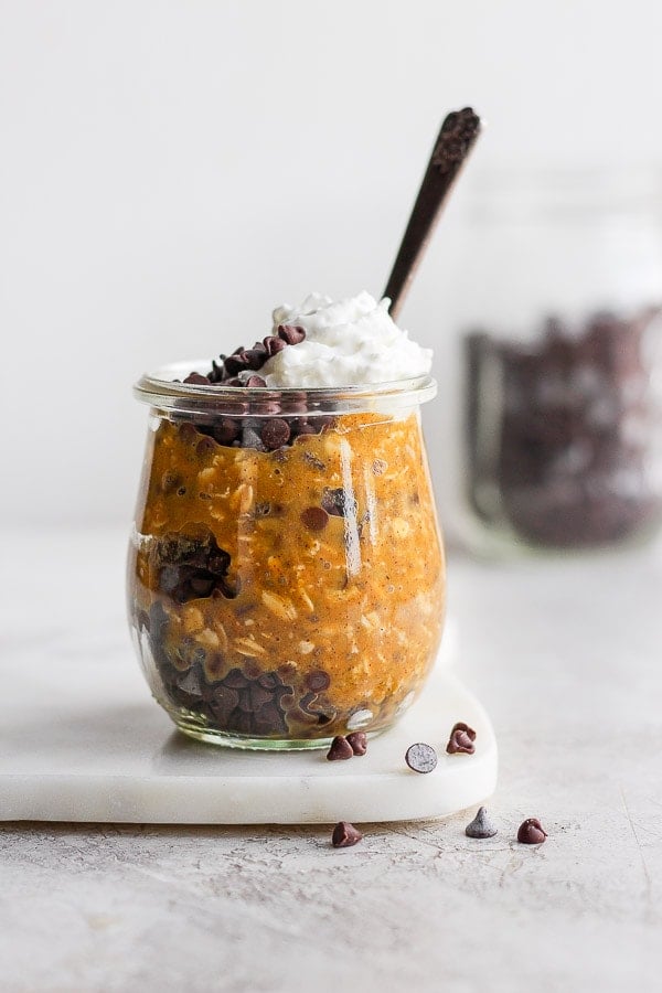 A small jar filled with chocolate chips and pumpkin overnight oats topped with dairy free whipped topping. 