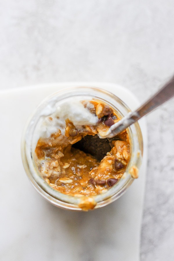 Top shot of a small jar filled with chocolate chips and pumpkin overnight oats topped with dairy free whipped topping. 