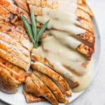 Smoked Turkey Breast on a plate, sliced, with gravy on top.