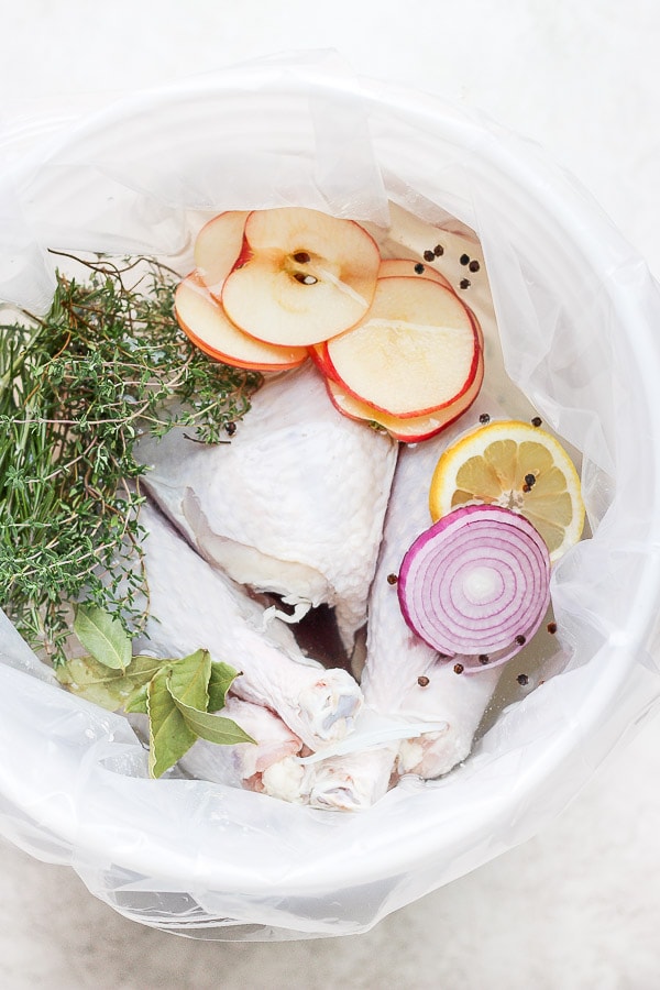 A large bucket with a brine bag in it with a raw turkey sitting in a brine with herbs, apples, onion and lemon. 