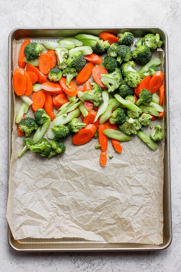 A parchment-lined baking sheet half covered with fresh vegetables.