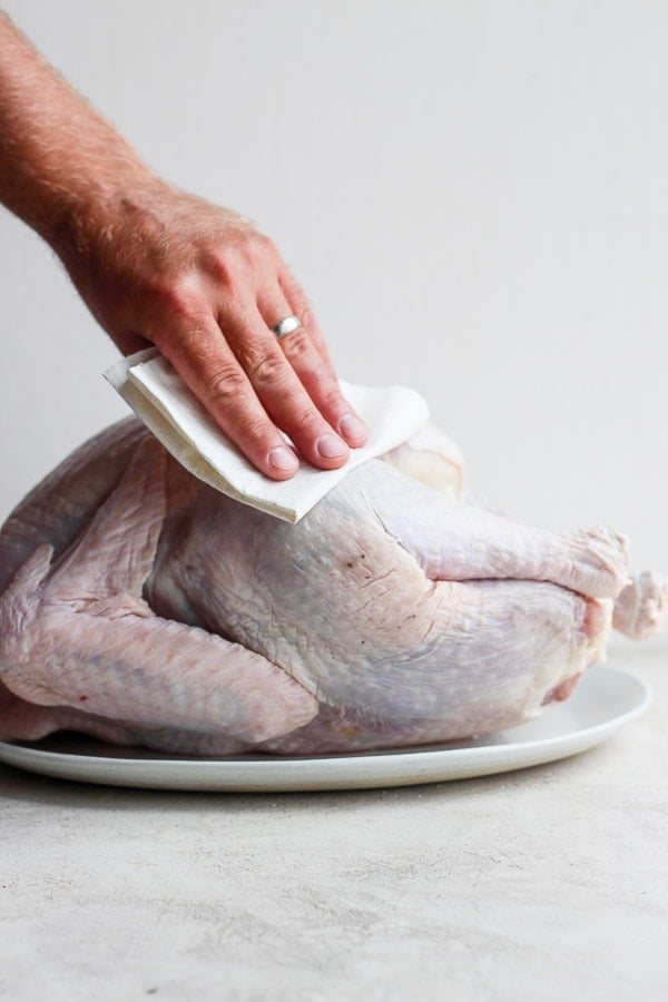 Male hand patting dry a raw turkey with clean paper towel. 