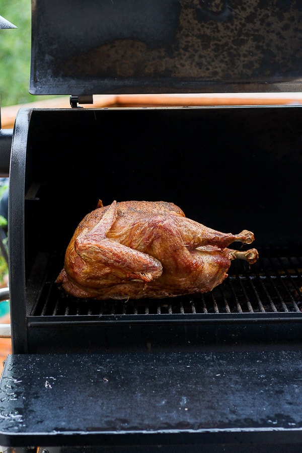 Cooked, whole turkey sitting on an open smoker. 