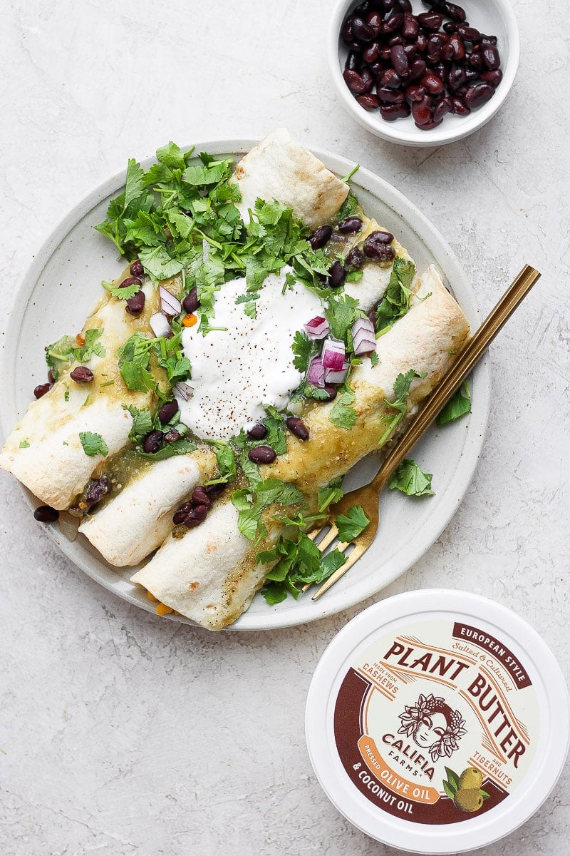 A plate with three vegan enchiladas topped with fresh cilantro, dairy free sour cream and red onions. 