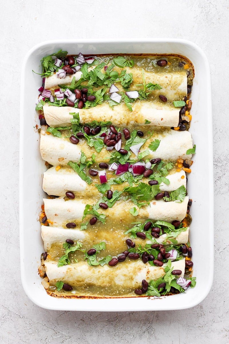 White casserole dish filled with cooked vegan enchiladas and topped with black beans and fresh cilantro. 