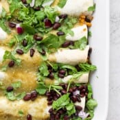 Several vegan enchiladas in a white baking dish and garnished with fresh cilantro.