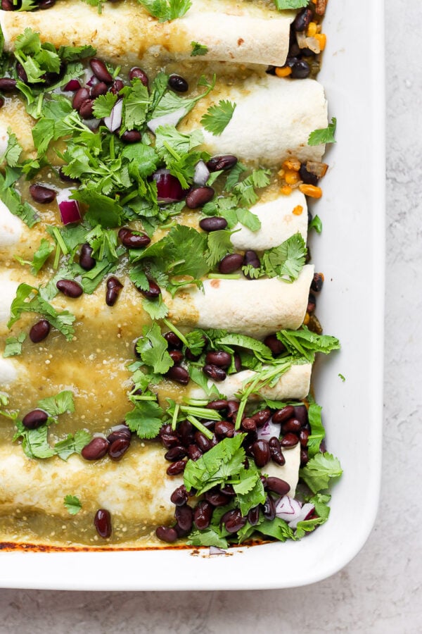 Several vegan enchiladas in a white baking dish and garnished with fresh cilantro.
