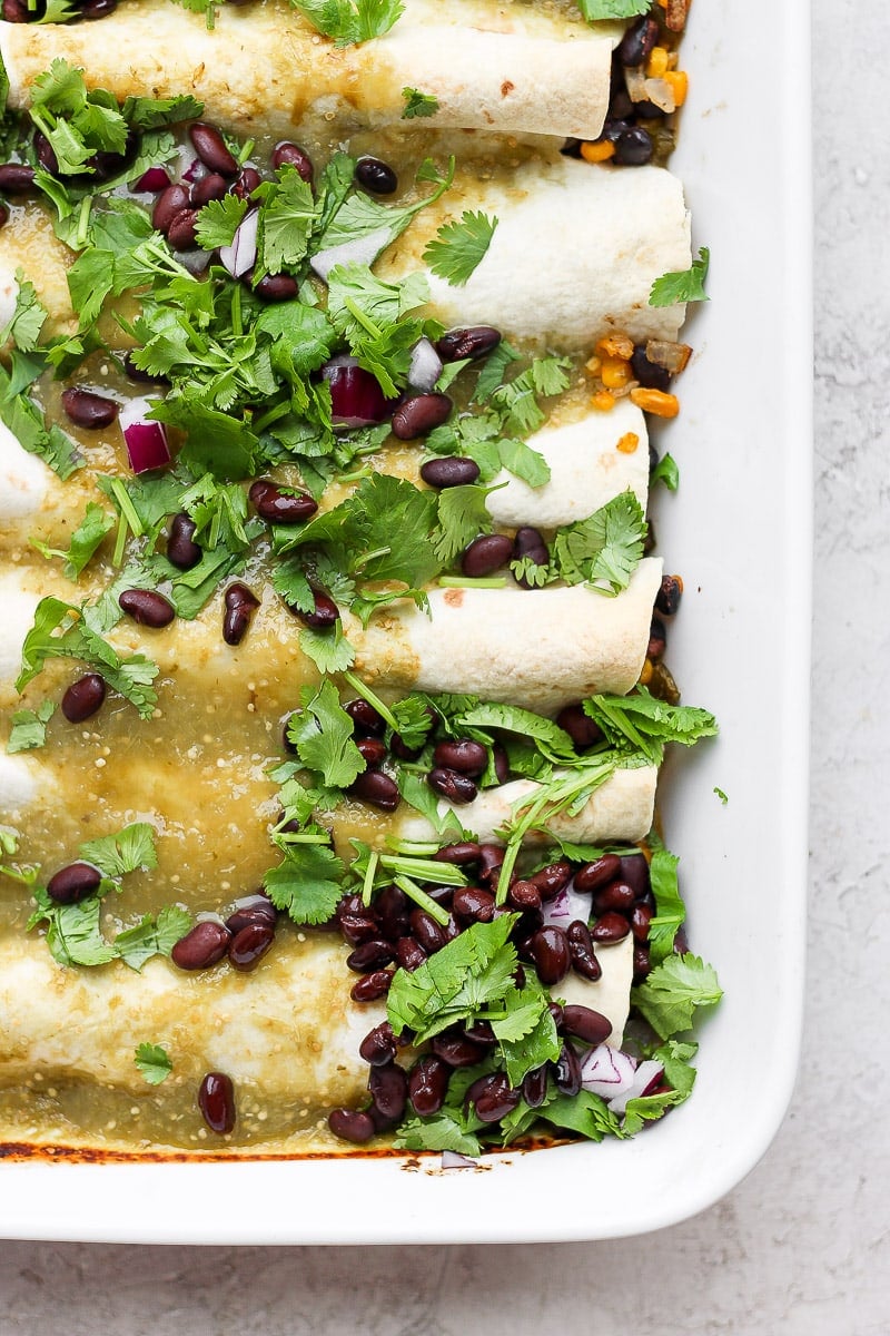 White casserole dish filled with cooked vegan enchiladas and topped with black beans and fresh cilantro. 
