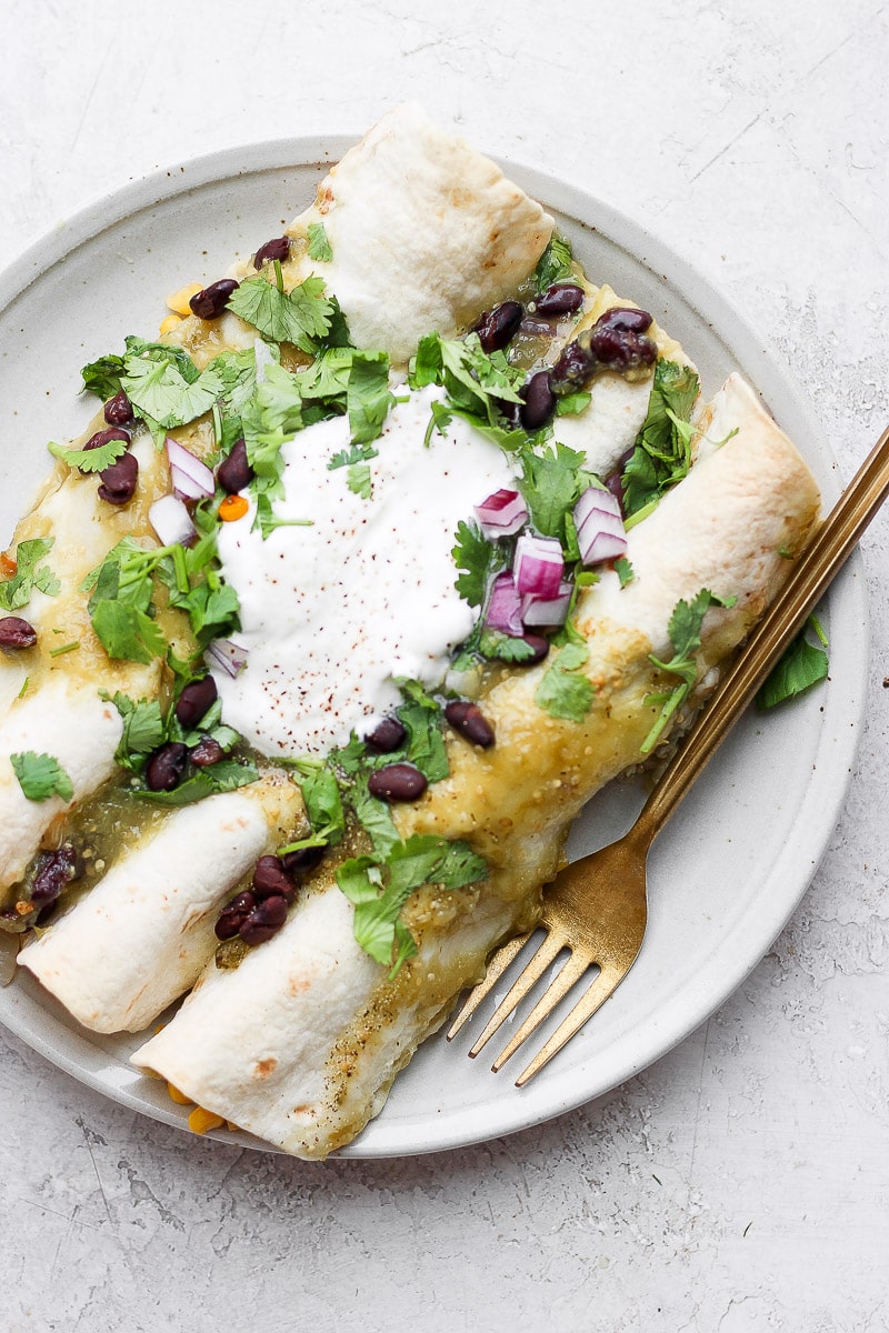 A plate with three vegan enchiladas topped with fresh cilantro, dairy free sour cream and red onions. 