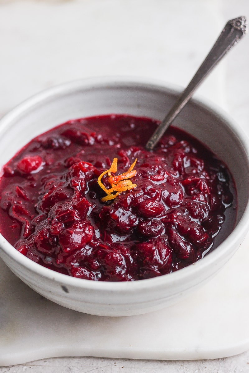 Cranberry orange sauce in a bowl with orange zest on top and a spoon sticking out. 