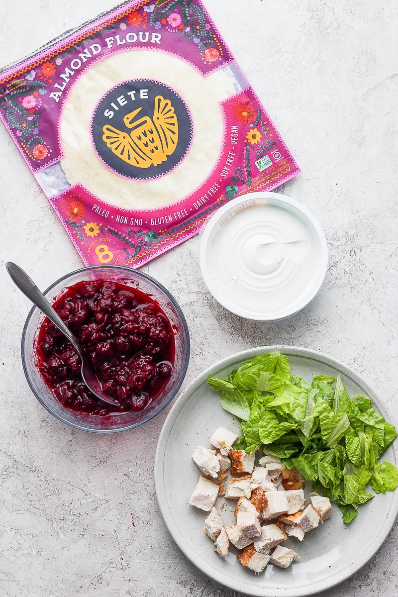 The ingredients for a turkey cranberry wrap - Siete tortillas, cranberry sauce, dairy-free cream cheese, romaine lettuce, and turkey.