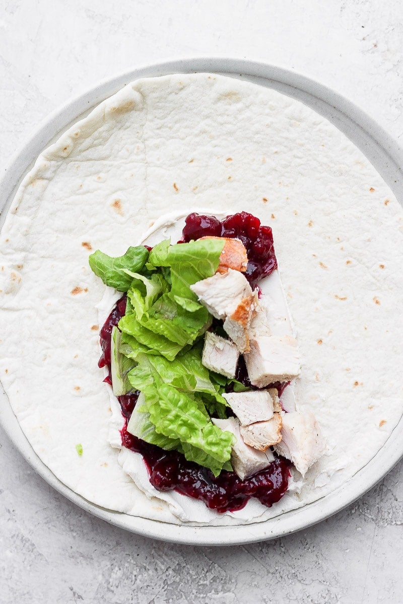 A tortilla with cranberry sauce, dairy-free cream cheese, romaine lettuce, and turkey.