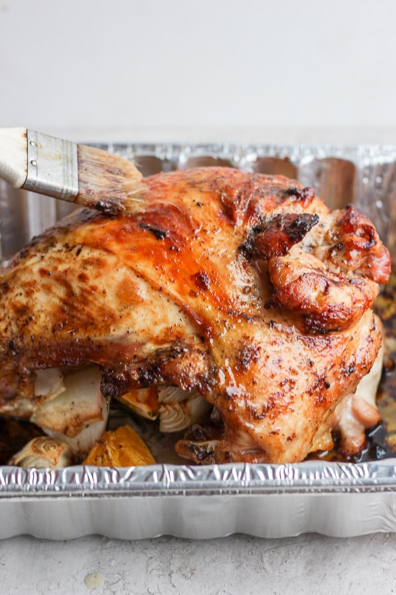 A cooked turkey breast being basted with drippings in an aluminum tray.
