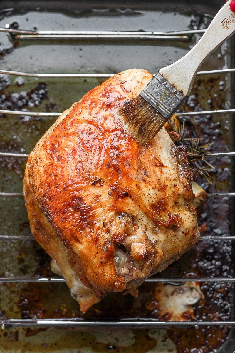 A cooked, brown turkey breast in a roasting pan and someone basting it with a brush. 