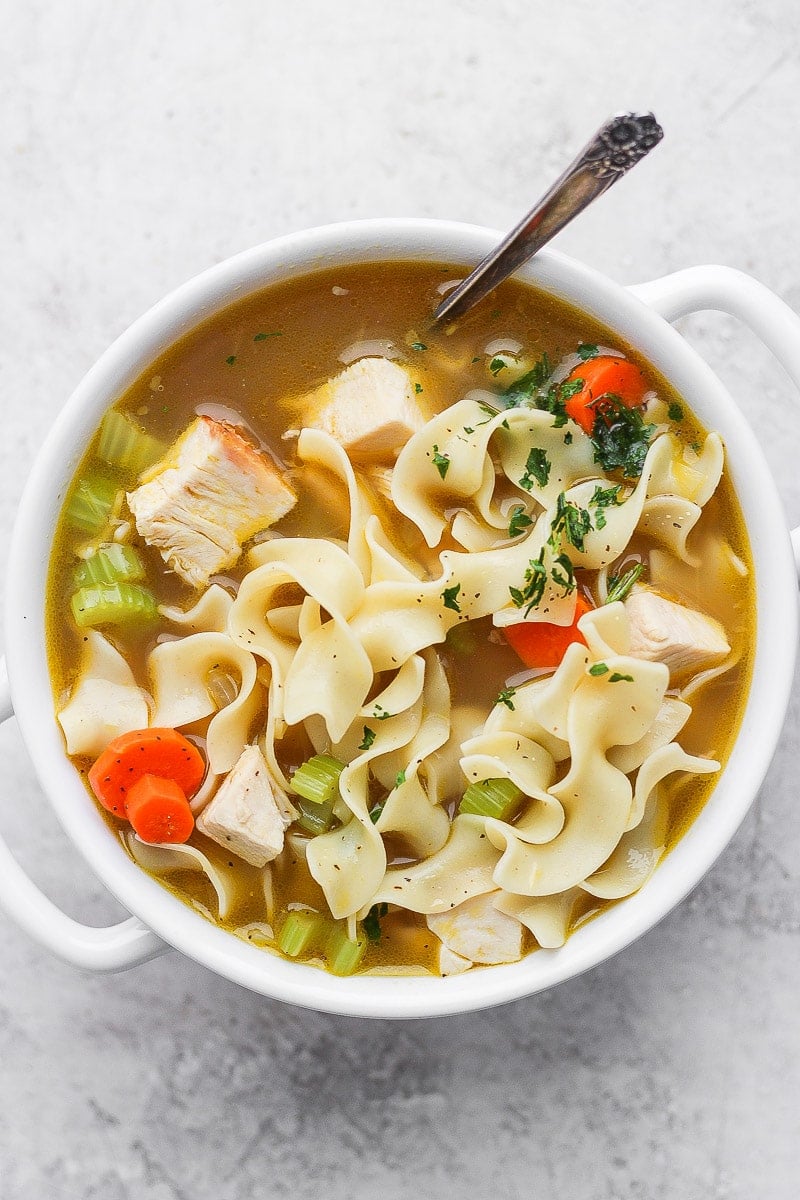 A bowl of leftover turkey noodle soup with a spoon.