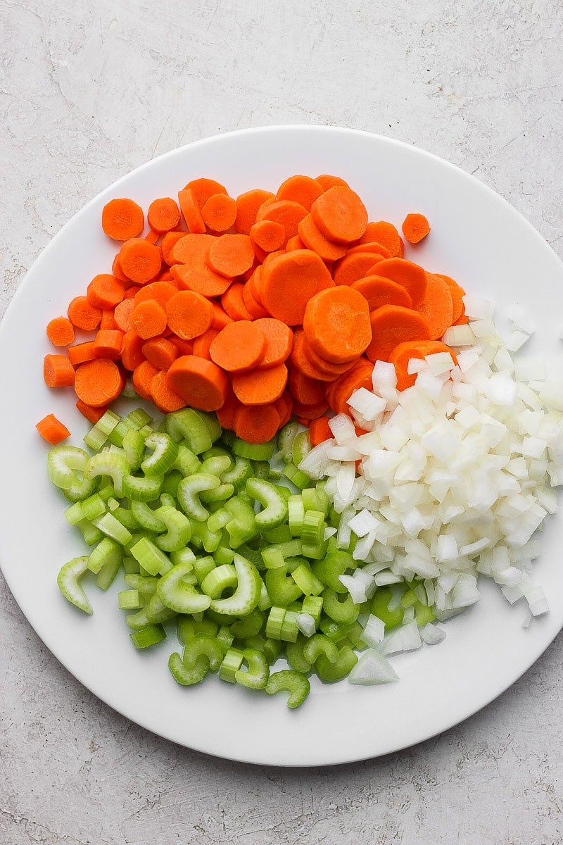 A white plate with chopped carrots, celery, and onions.