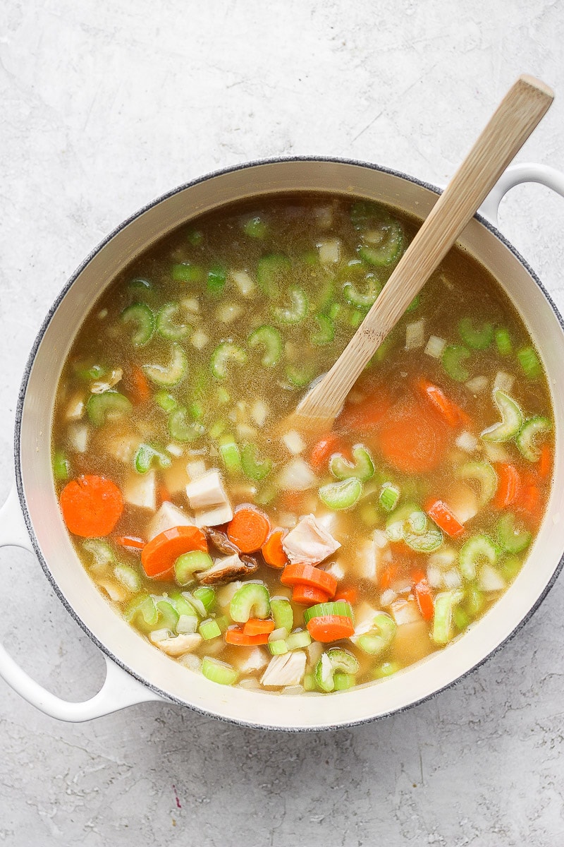 A large pot with cooked carrots, celery, onions, turkey, parsley, and broth.