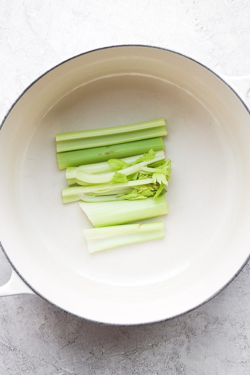 Dutch oven with a few pieces of celery sitting in the bottom of the pan. 