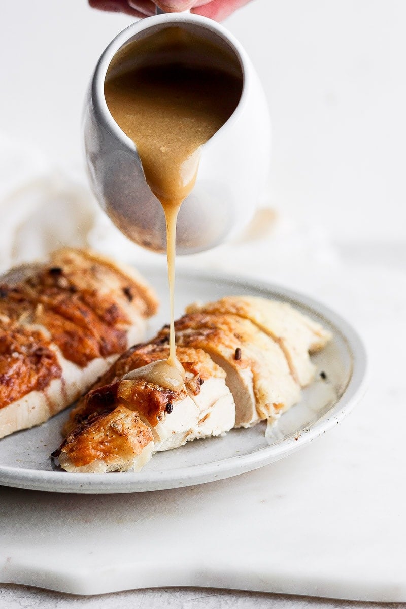 Gravy being poured on top of a chicken breast. 