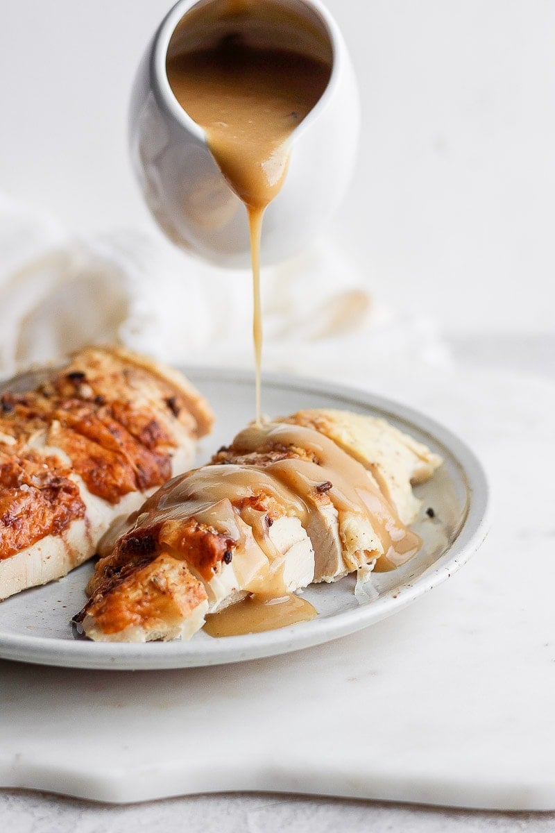 Gravy being poured on top of a chicken breast. 